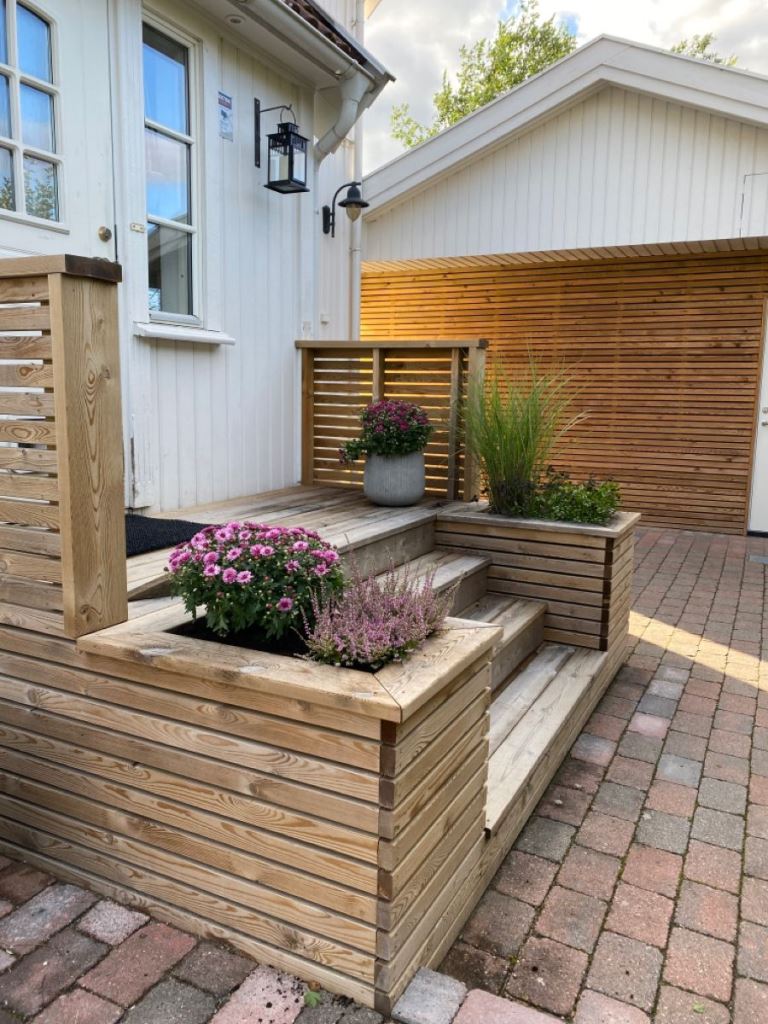 The small porch features a wooden staircase with built-in planters, with flowers and greenery.