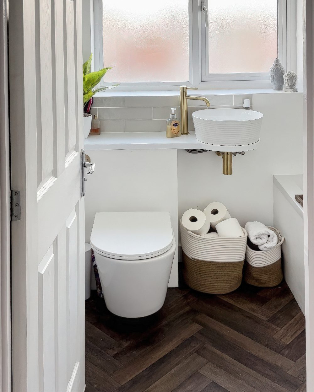 This modern small bathroom makes the most of its limited space with a sleek wall-mounted toilet, a minimalist white vessel sink, and a compact countertop. The brass faucet is a stylish touch.

(@theneutralfamilyhome).