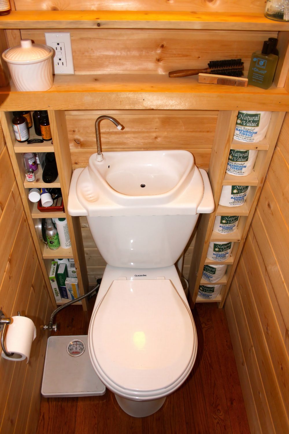 A tiny cottage bathroom that features a porcelain toilet/sink combo and an open shelving unit.