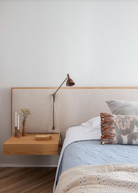 The airy space is done with a bed and an added upholstered headboard with a nightstand and wall lamp attached.