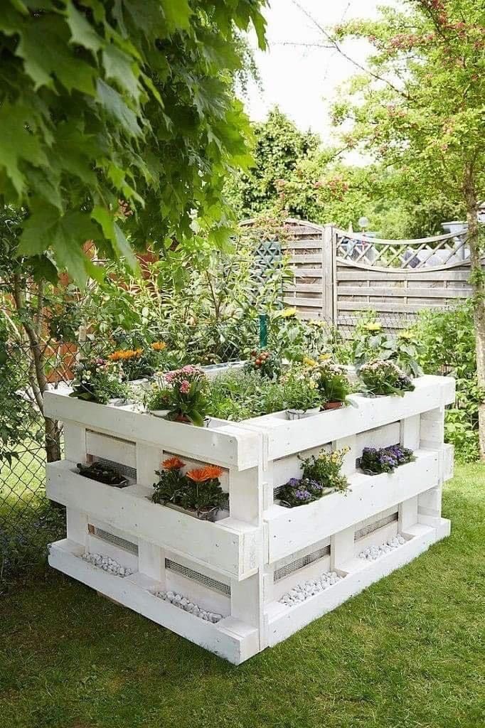 This pallet garden is shaped as a cube, with plant stands and a garden bed in the center.